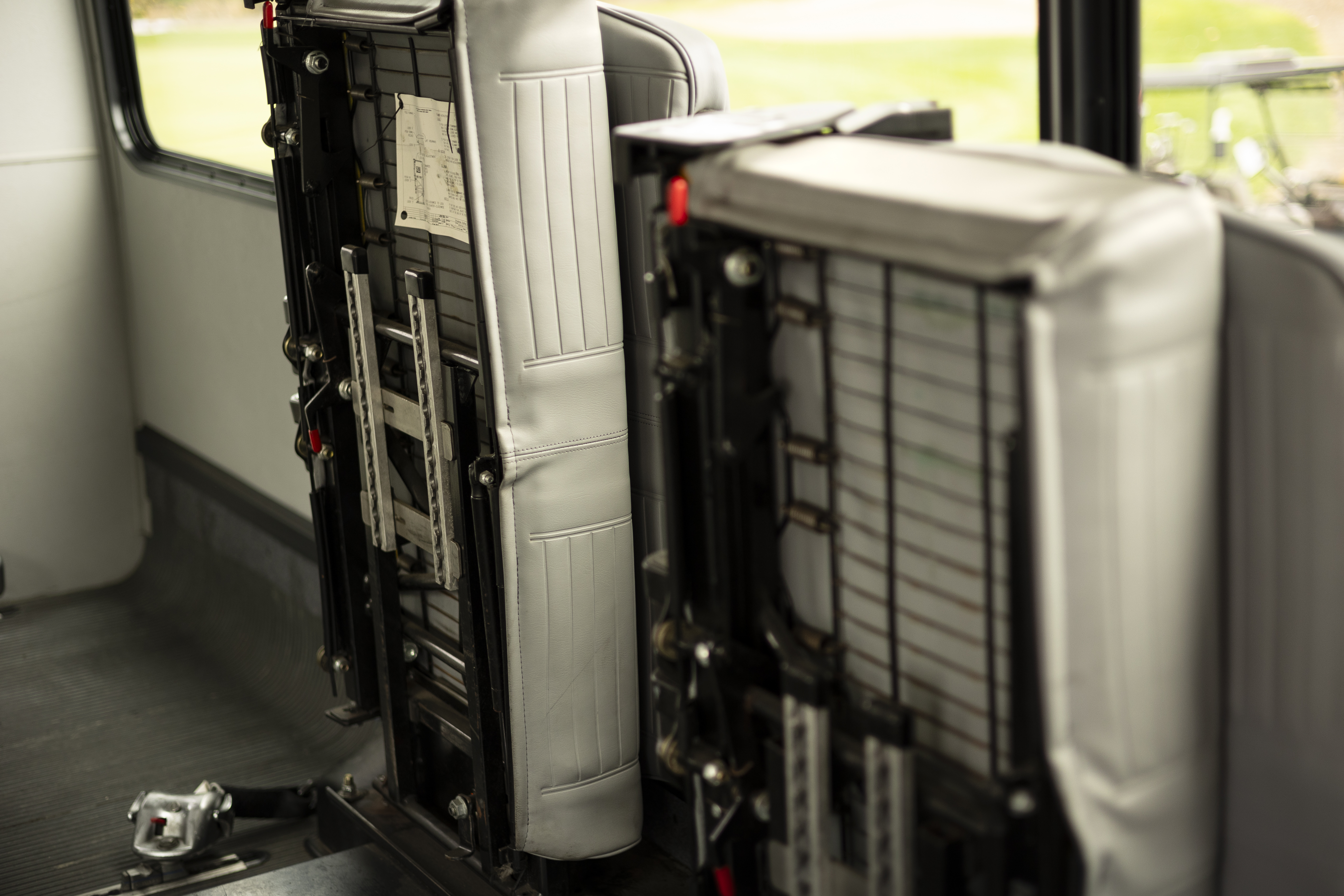 Two vehicle bench seats are pictured lifted vertically and secured into place, making more space in the back of a Ford E-350 cutaway with mobility van upfits.